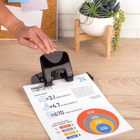 Built Different Two Hole Punch Crushes Twenty Sheets Like Nothing Else With Smart Touch Low Effort Grip And Tight Accuracy Alignment Track For Quick Paper Organizing Jobs In Sleek Black Gray being used on a document.