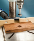 Dust Right Port for Drill Press Fence Portable Dust Collection Attachment with upward angled hose and wood piece on a drill press
