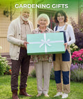 Three people standing in a garden holding a large green gift box with a ribbon labeled 'Gardening Gifts' in front of a house.