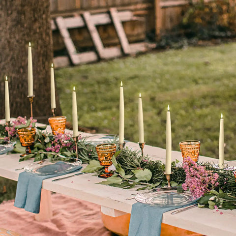 Flameless Taper Candles Set With Realistic 3D Flame And Wick, 9-Inch Ivory Wax LED Candles, 10 Pack displayed on outdoor table.