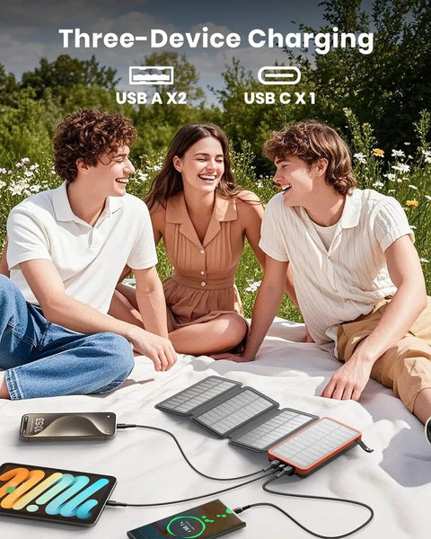 Group of people using Outdoor Solar Charger 25000mAh with Four Solar Panels USB C Power Bank for multiple devices on grass.