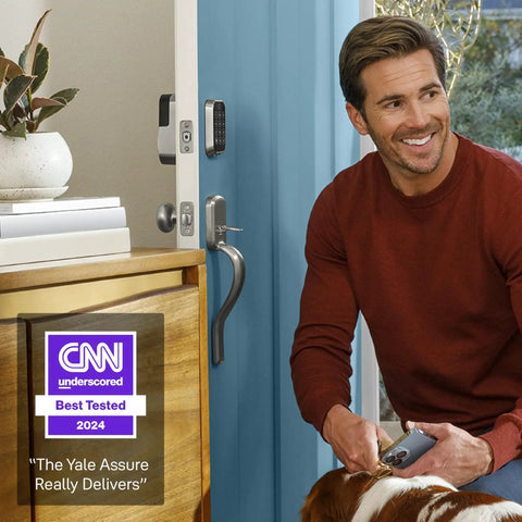 Man using Assure Lock 2 Deadbolt Keyless Door Lock With Satin Nickel Finish and touchscreen keypad on front door, holding phone.