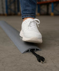Person stepping on D-2 Rubber Duct Cord Cover 36 Inch Gray Floor Cable Protector for power cables ethernet coax phone lines and more.