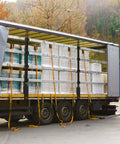 Truck loaded with industrial materials secured by straps, parked outdoors near a forest during fall season.