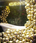 Top Tier 12 Inch Gold Latex Helium Balloons 50 Pack Slay Party Decorations displayed in a decorative arrangement near a bathtub.