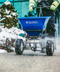 Walk Behind Universal Spreader With 100 Lb Capacity For Seed Fertilizer Salt Ice Melt, 13 Inch Pneumatic Tires, shown on snowy path