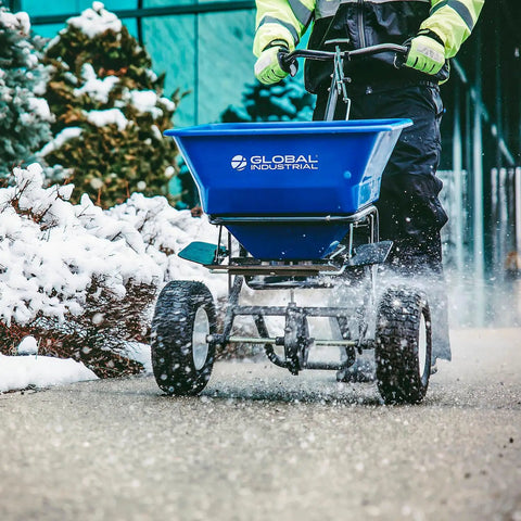 Walk Behind Universal Spreader With 100 Lb Capacity For Seed Fertilizer Salt Ice Melt, 13 Inch Pneumatic Tires, shown on snowy path