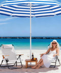 Premium Portable Camping Chair With 5-Position Recliner in cream white on a beach, next to a smiling woman under a striped umbrella.