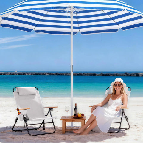 Premium Portable Camping Chair With 5-Position Recliner in cream white on a beach, next to a smiling woman under a striped umbrella.