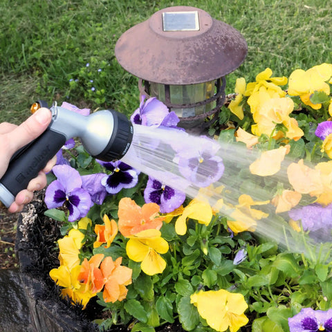 Person using Small Metal Garden Hose Nozzle With Seven Spray Patterns to water a colorful flower bed