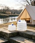 10L Collapsible Water Container With Spigot For Camping And Hiking set in outdoor camping scene by a tent and river.