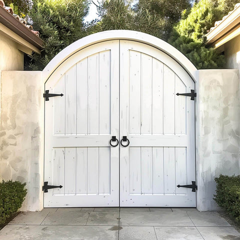 White wooden garden gate with black hinges and handles, surrounded by greenery and stone walls in an outdoor setting.
