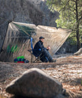Camper sitting beside Tough As Nails Heavy Duty Survival Blanket With Reflective Thermal Layer For Camping And Outdoor Gear Waterproof Tarp.