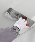 Pro Grade Drywall Finish Trowel With Stainless Steel Blade And Ergonomic Grip used on drywall surface by gloved hand