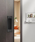6 Inch Flush Pull Sliding Barn Door Handle Set on wooden door, recessed rectangular plate in matte black, installed, room background
