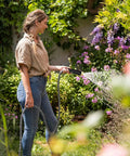 Garden hose in use: black 50-ft hose with spray nozzle, side view of a woman watering a lush garden.