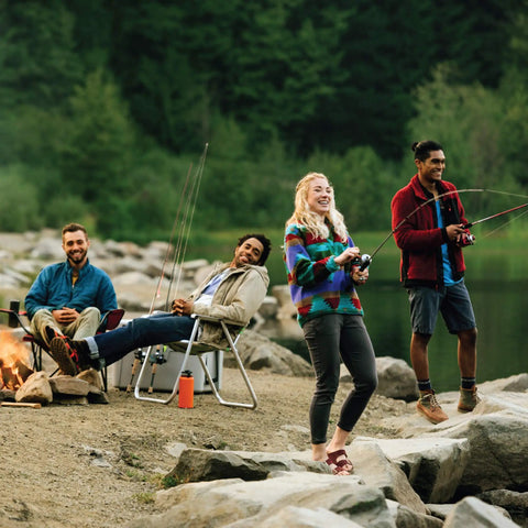 Four people fishing with Spincast Reel And Fishing Rod Combo, 7 Foot Two Piece Rod With Size 80 Reel, near a campfire by a lake.