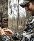 Hunter setting up Edge 2 Cellular Trail Camera With Nationwide 4G LTE Auto Connect on tree, using smartphone for easy setup.