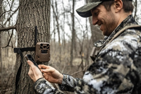 Hunter setting up Edge 2 Cellular Trail Camera With Nationwide 4G LTE Auto Connect on tree, using smartphone for easy setup.
