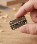 Close-up of 12 Pack Small Iron Hinges With Rounded Corners 1.4 Inch Antique Bronze Cabinet Butt Hinges in a hand