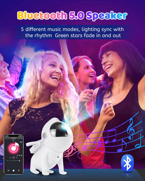 Lit Cosmic Night Sky Projector with Bluetooth speaker next to dancing group, showcasing app control and night light features.