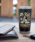 Tumbler with vintage go-kart racing design on a table beside a wallet and smartphone.