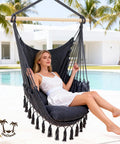 Woman sitting in a hammock hanging chair with two cushions, portable Caribbean style swing seat for outdoor and indoor use, 500 lb capacity, lightweight dark grey, cloud like comfort for beach, patio or travel.