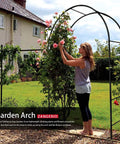 Woman arranging flowers on Sturdy Garden Arch Trellis For Climbing Plants Outdoor Wedding Arches Ceremony Decor Black Metal Garden Arbor 7.9 Ft Wide By 6.4 Ft High