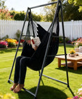 Relaxing in a black Ultra Cozy Hammock Chair Set with foldable anti-tip stand, outdoors in a garden, 450 lb capacity.