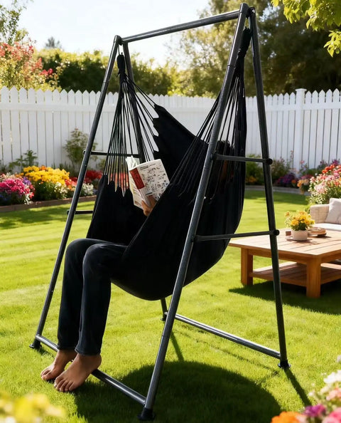 Relaxing in a black Ultra Cozy Hammock Chair Set with foldable anti-tip stand, outdoors in a garden, 450 lb capacity.