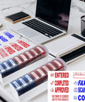 Top Tier Self Inking Office Stamp Set With Eight Gotta Have Rubber Phrases Like Paid And Approved on a desk with laptop.