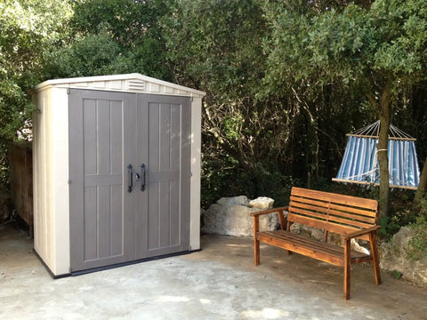 Factor 6x3 Outdoor Storage Shed Kit For Patio Furniture Lawn Tools Bikes Beach Gear Plus More Durable Resin Construction in Taupe and Brown next to bench and hammock