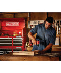Man using V20 Cordless Impact Driver Kit with 1/4 Inch Quick Release Chuck in workshop, red toolbox behind.