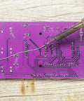 Noob Friendly Soldering Practice Kit for DIY Electronics Projects Learn to Solder with Detailed Circuit Schematics and Hands On STEM Education for Starters featuring purple circuit board with soldering iron tip in action.