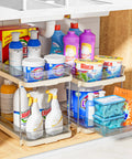 No Fuss Slide Out Two Tier Under Sink Organizer With Reconfigurable Dividers Stackable Pantry Storage Rack In Warm Beige loaded with cleaning supplies.