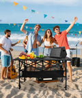 Folding Camping Table With Roll Up Top Height Adjustable Portable Metal Camp Table For Picnic Or Cookout Oversized 37.4 Inch Surface Mesh Storage Basket Carry Bag Included For Beach Backyard Or Party on a beach with people enjoying a day out.