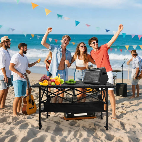 Folding Camping Table With Roll Up Top Height Adjustable Portable Metal Camp Table For Picnic Or Cookout Oversized 37.4 Inch Surface Mesh Storage Basket Carry Bag Included For Beach Backyard Or Party on a beach with people enjoying a day out.