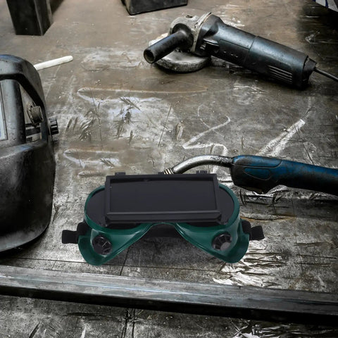 Heavy Duty Flip Up Welding Goggles resting on a workshop table, showcasing anti-scratch design and impact-resistant features.