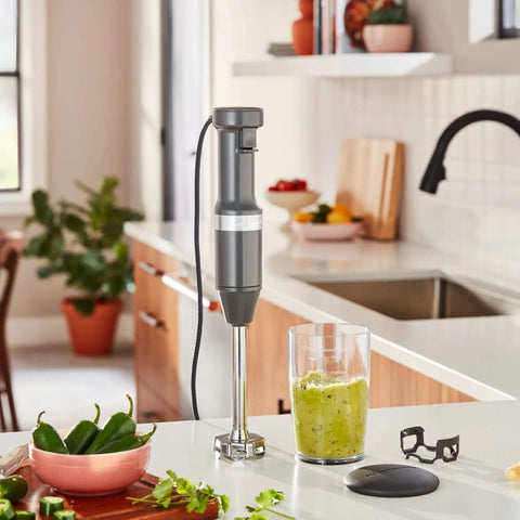 Total Kitchen Workhorse Variable Speed Corded Hand Blender With Removable Eight Inch Arm and Sharp Stainless Blades For Blending Soups And Making Smoothies Using Quick Trigger Controls In Sleek Charcoal Grey with a blending jar on a kitchen counter.