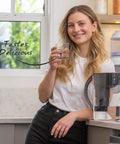 Smiling woman holding a glass of water next to a pitcher using Replacement Alkaline Water Filter For At Home Pitcher With Mineral Boost.