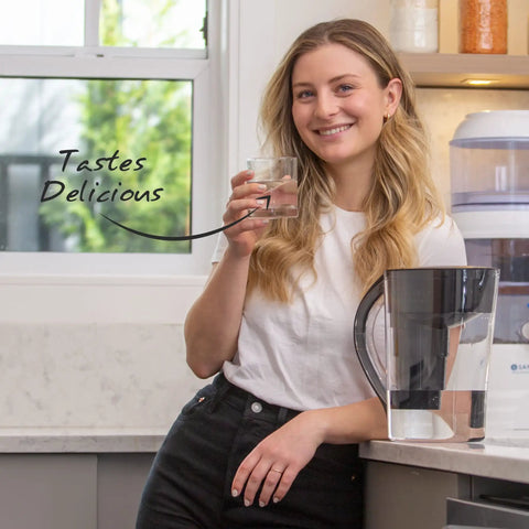 Smiling woman holding a glass of water next to a pitcher using Replacement Alkaline Water Filter For At Home Pitcher With Mineral Boost.