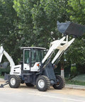Powerful 4WD Backhoe Loader With 2.5 Meter Digging Depth, Loader Bucket raised, shown on construction site with trees