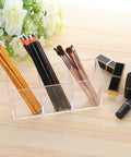 Clear Acrylic Silverware And Pen Organizer Caddy For Office And Home, displaying pencils and brushes on a wooden surface.