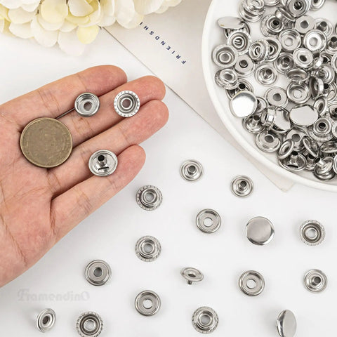 Hand holding components of 200 Pack Stainless Steel Snap Fastener Kit 15mm Heavy Duty Button Press Stud Caps For Marine Boats Canvas Leather Bags And DIY Crafts Ideal For Tent Covers Jackets Coats Vests Tops And More, spread on table.