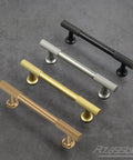Four metal cabinet pulls in different finishes including champagne bronze, arranged on a gray surface, showcasing design and style.