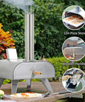 12-Inch Multi-Fuel Outdoor Pizza Oven with stainless steel body and wooden handle, installed on outdoor table in backyard setting.