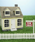 Miniature yellow dollhouse with a white picket fence and 'For Sale' sign on grass. Perfect for Fairy Gardens landscaping.