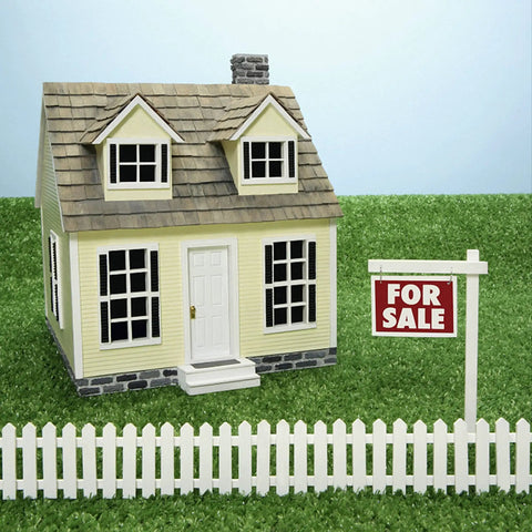 Miniature yellow dollhouse with a white picket fence and 'For Sale' sign on grass. Perfect for Fairy Gardens landscaping.