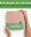 Hands holding a box of IslandMat Wetsuit Changing Mat, gift-ready for surfers, with text promoting 2 in 1 Gear Bag With 5000X Waterproof Tech.