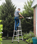 9.5 Foot Telescoping Aluminum Ladder A Frame Grab And Go Portable Extension Ladder For Home Roof Stairs Indoor And Outdoor Use 330 Pound Load Capacity No Assembly Required Lightweight And Easy to Carry. Man using A-frame ladder by house